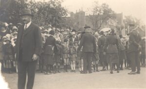 Postcard showing a crowd lining the street for the opening of Weybridge Hospital by Princess Beatrice, 27th June 1928. There is a row of Brownies at the front of crowd. This is one such event for the Brownies which would have been seen as 'serving the King' and the country.